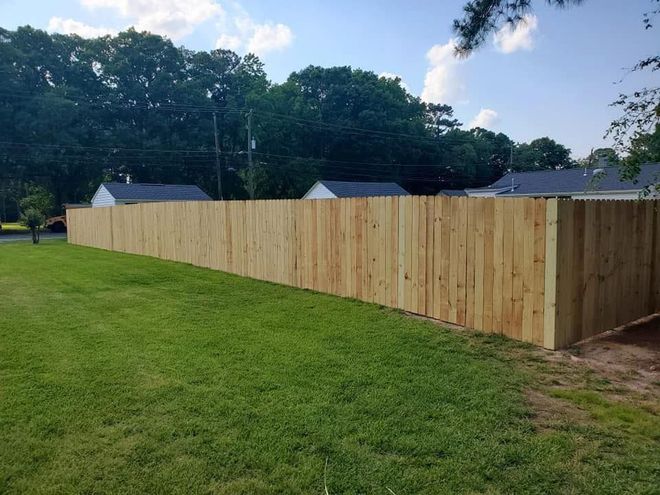 Long wooden privacy fence along a grassy yard at dusk with trees and rooftops in the background