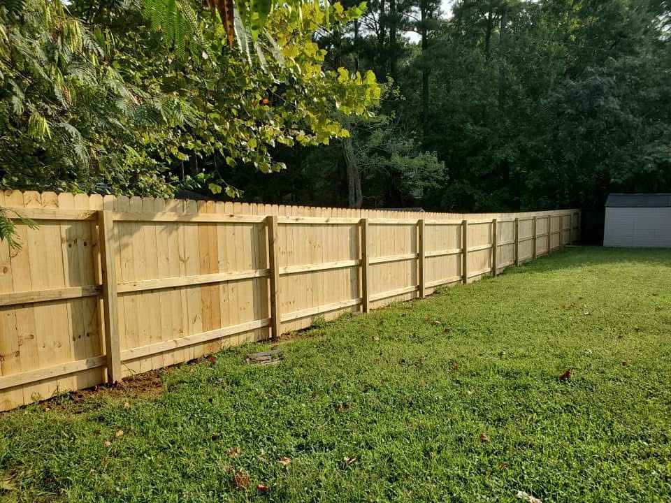 Wooden privacy fence along a grassy backyard, with trees and a shed in the background.