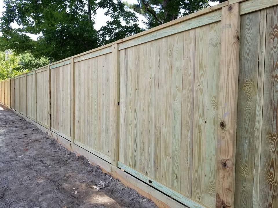 Long wooden privacy fence along a dirt path under trees