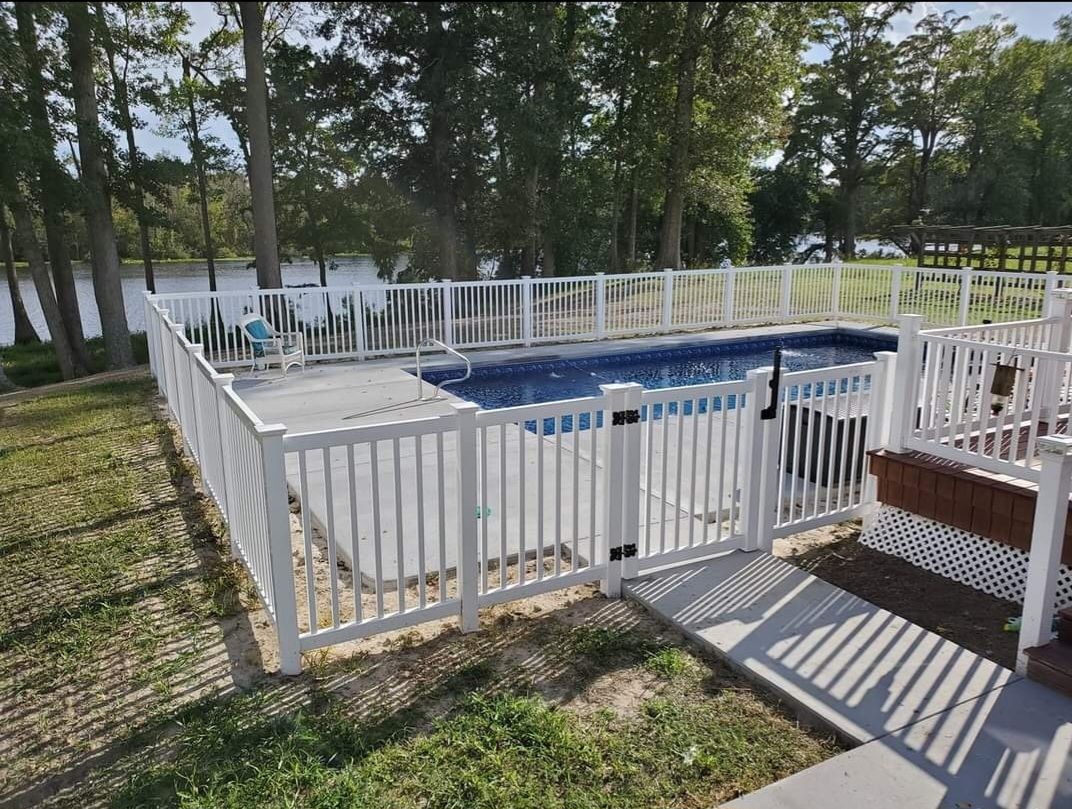 Fenced backyard pool with blue water, white railing, and trees in the background