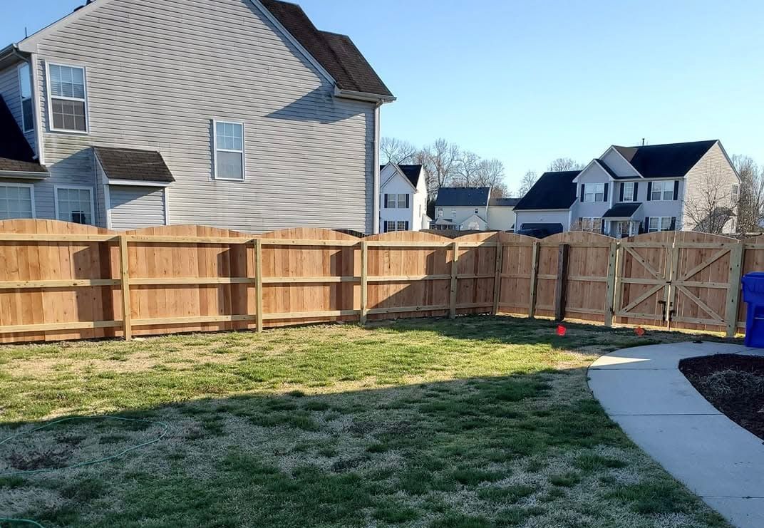 Backyard with wooden fence, grass lawn, and a curved concrete path beside suburban houses