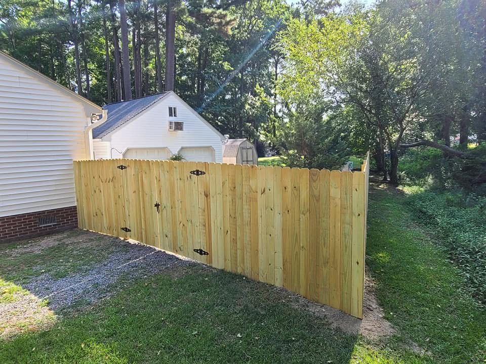 Wooden privacy fence in a grassy backyard beside a white house and trees