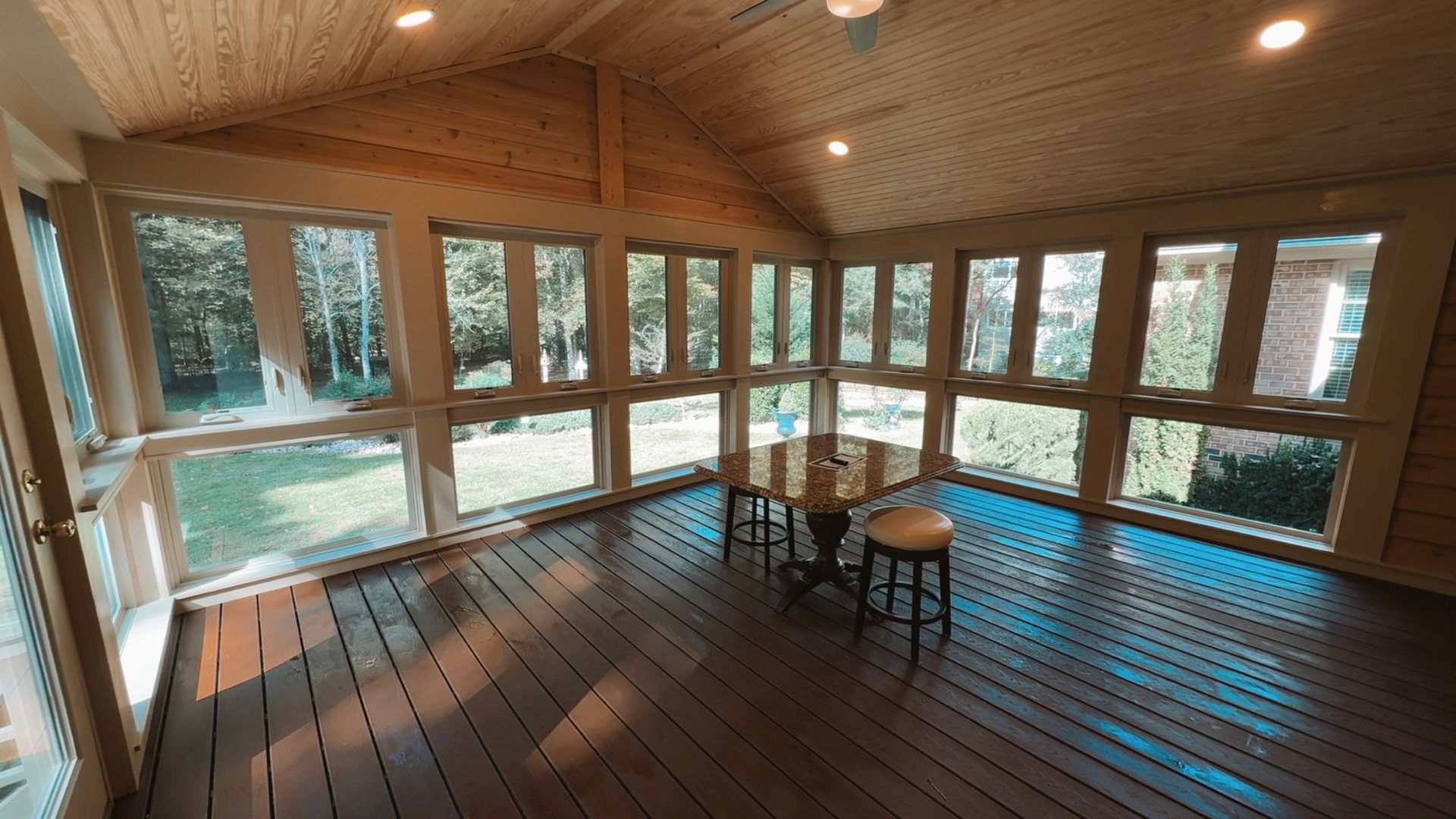 Sunlit screened porch with wooden floor, wicker table, and chairs overlooking snowy trees