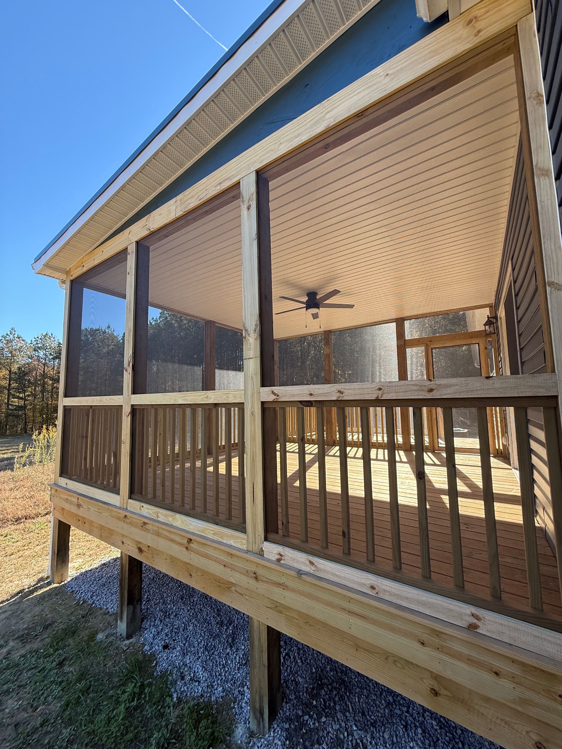 Wooden screened porch with railing and ceiling fan under a sunny blue sky