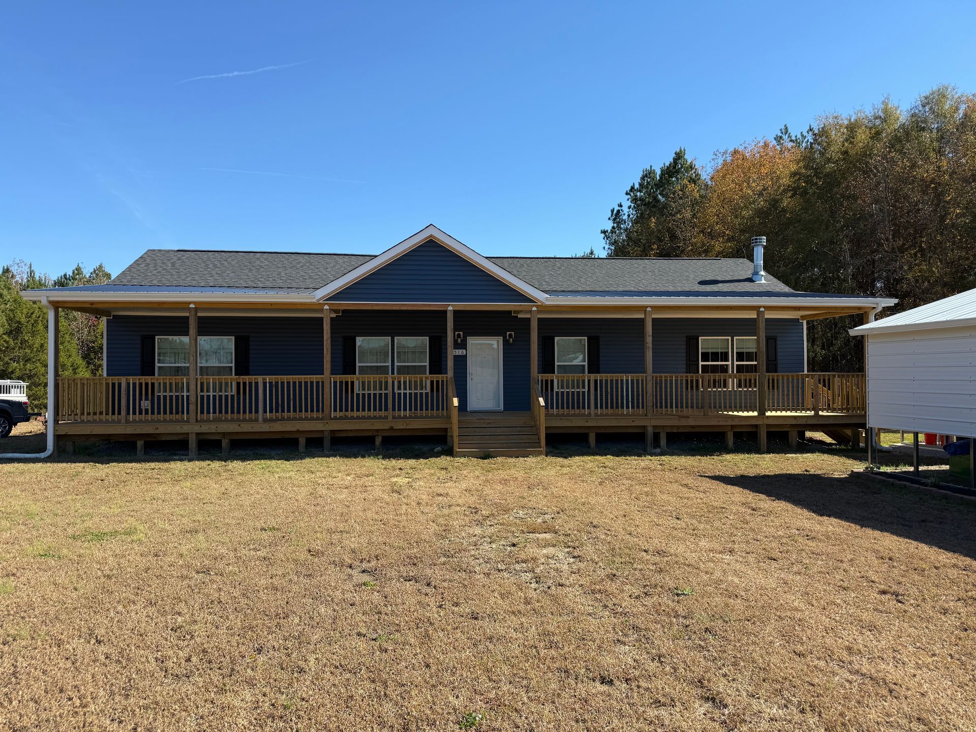 Single-story house with a front porch, gray roof, and dry yard under a clear blue sky