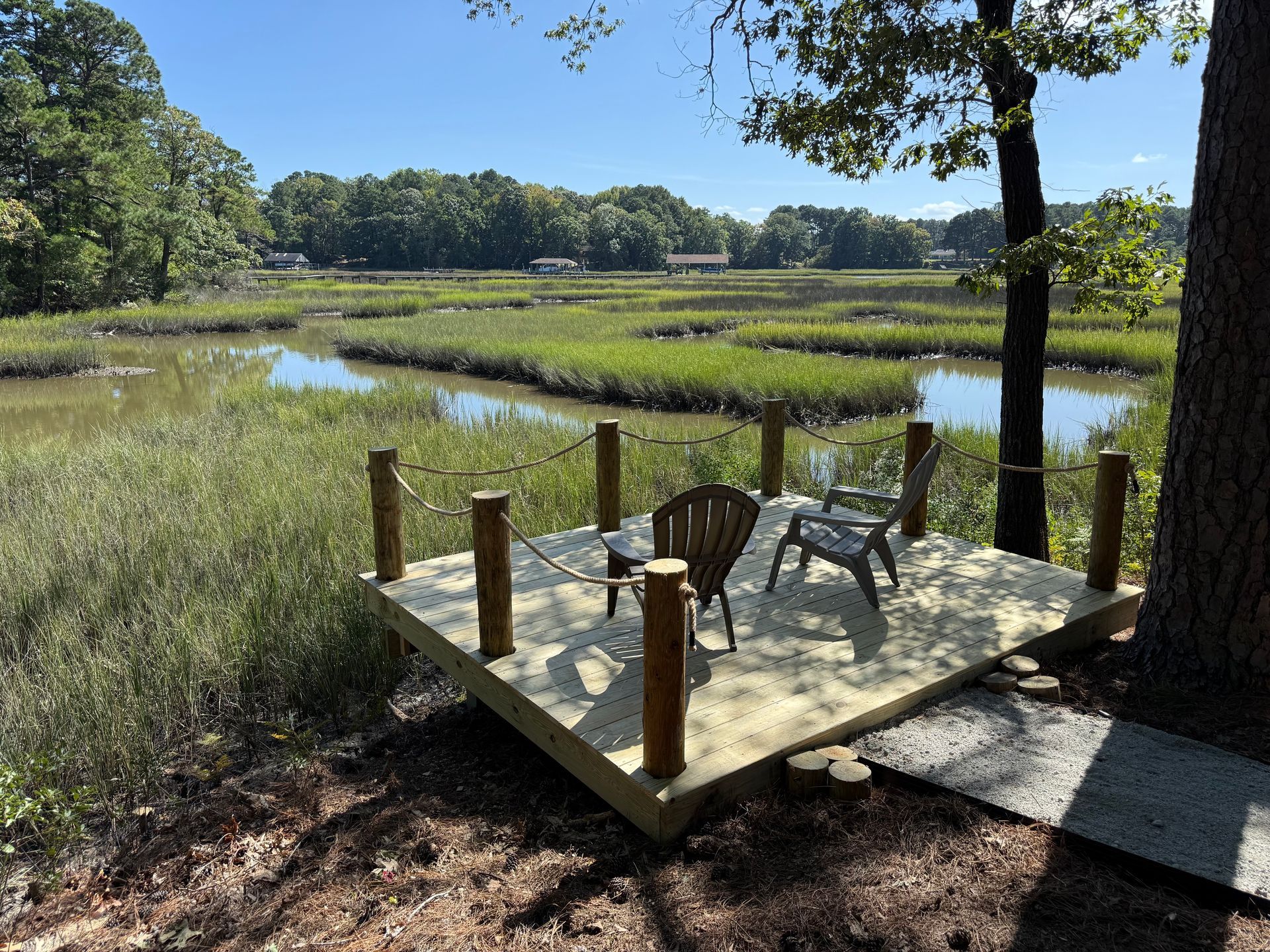 Wooden dock with chairs overlooking a marsh pond under bright blue sky