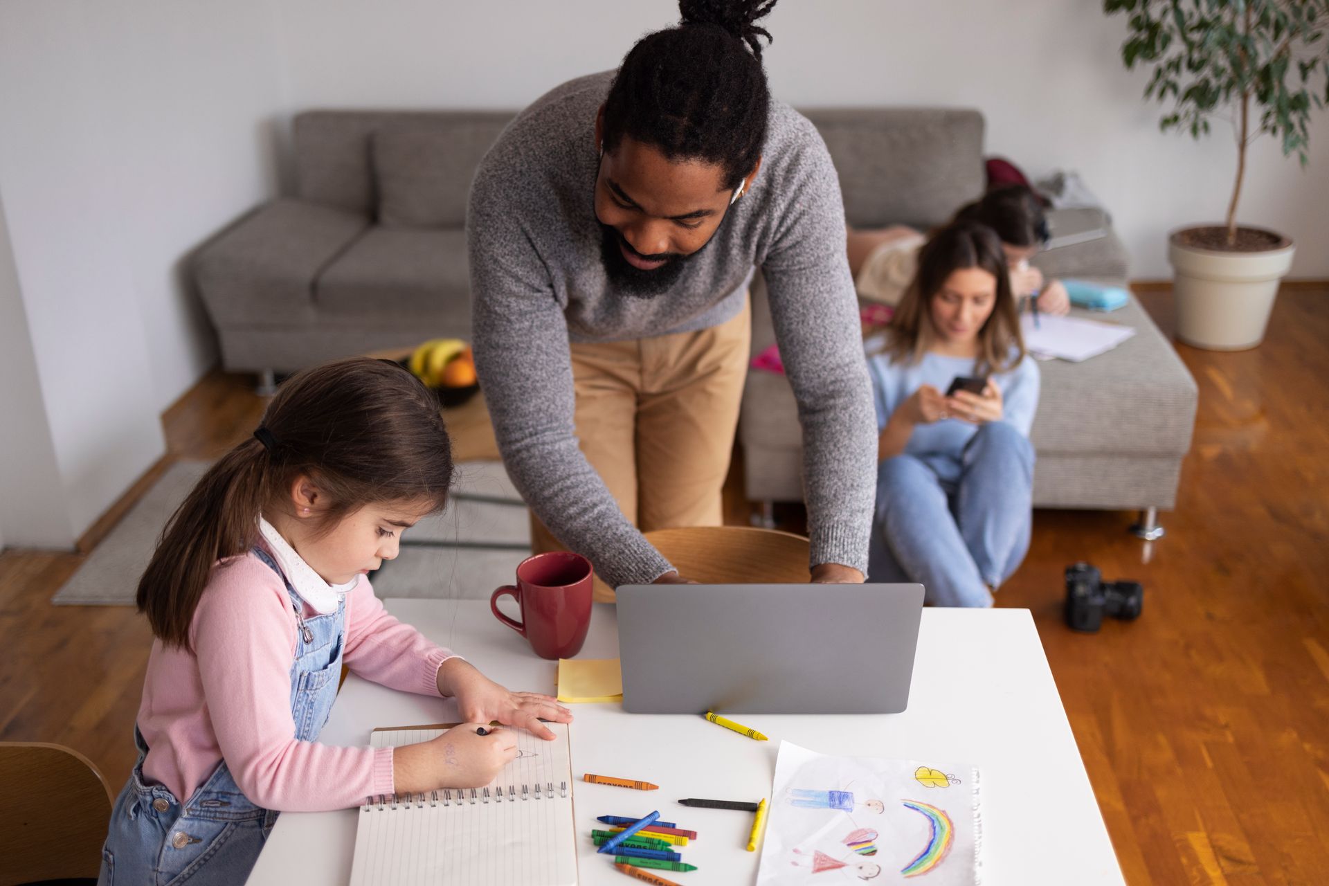 A man is helping a little girl with her homework in a living room.