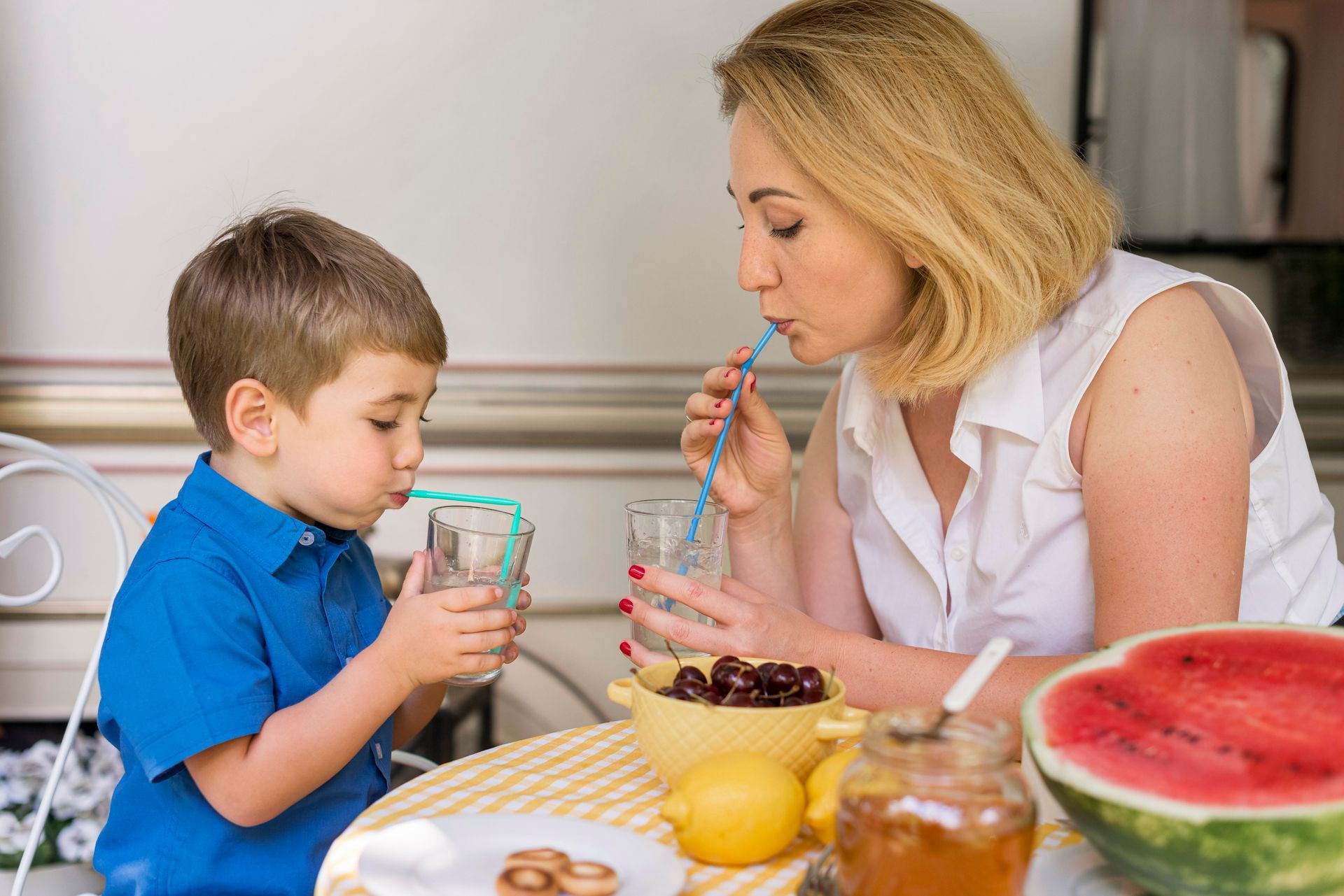 A woman and a child are sitting at a table drinking water through a straw.