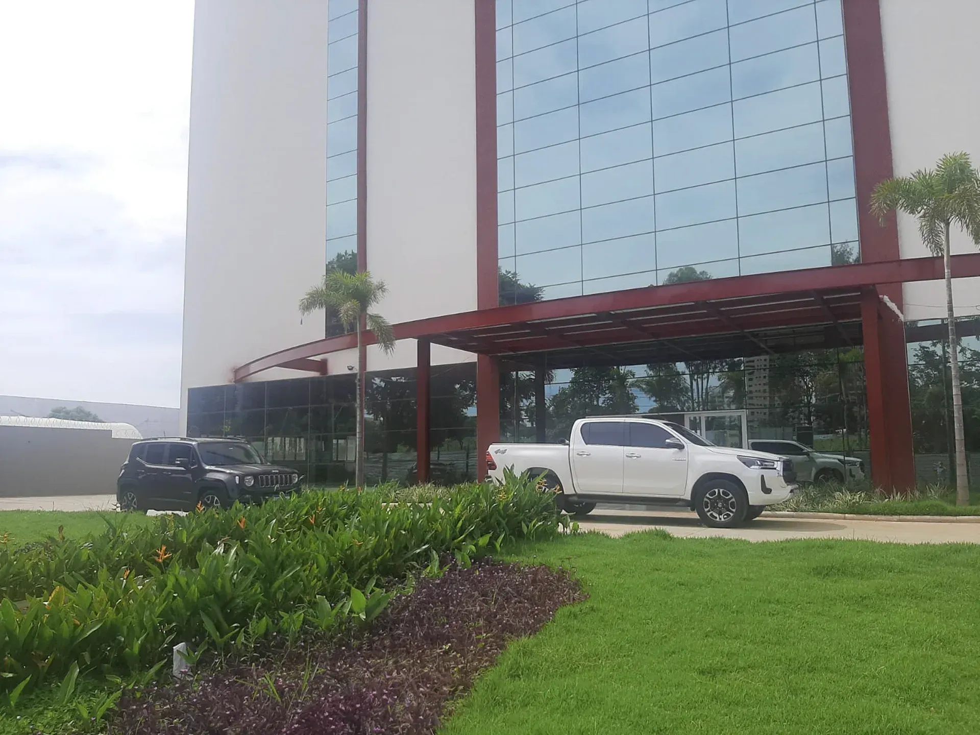 Uma caminhonete branca e um carro preto estacionados em frente a um prédio moderno com janelas de vidro.