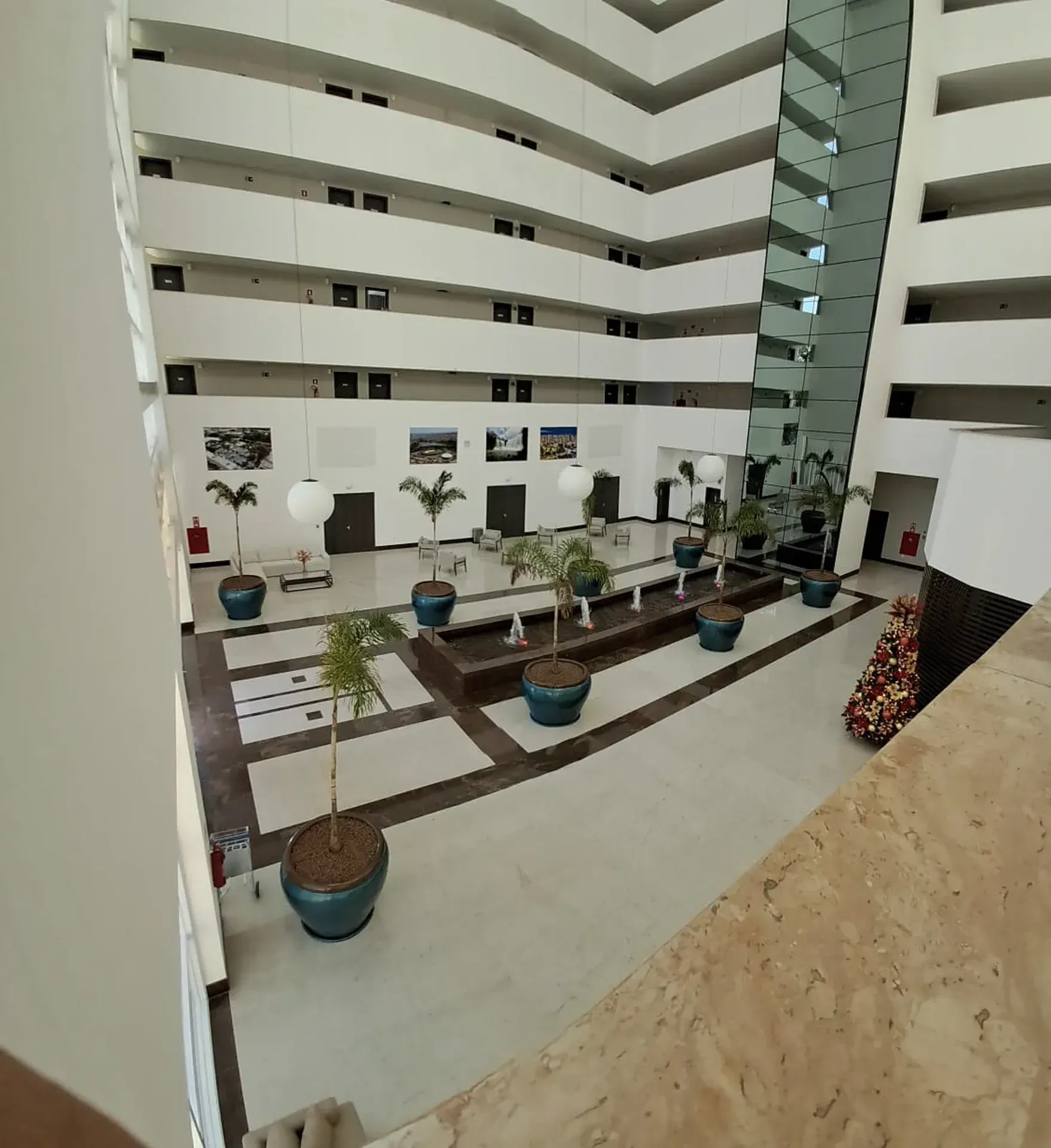 Átrio interno do hotel com várias varandas, plantas e grandes janelas.