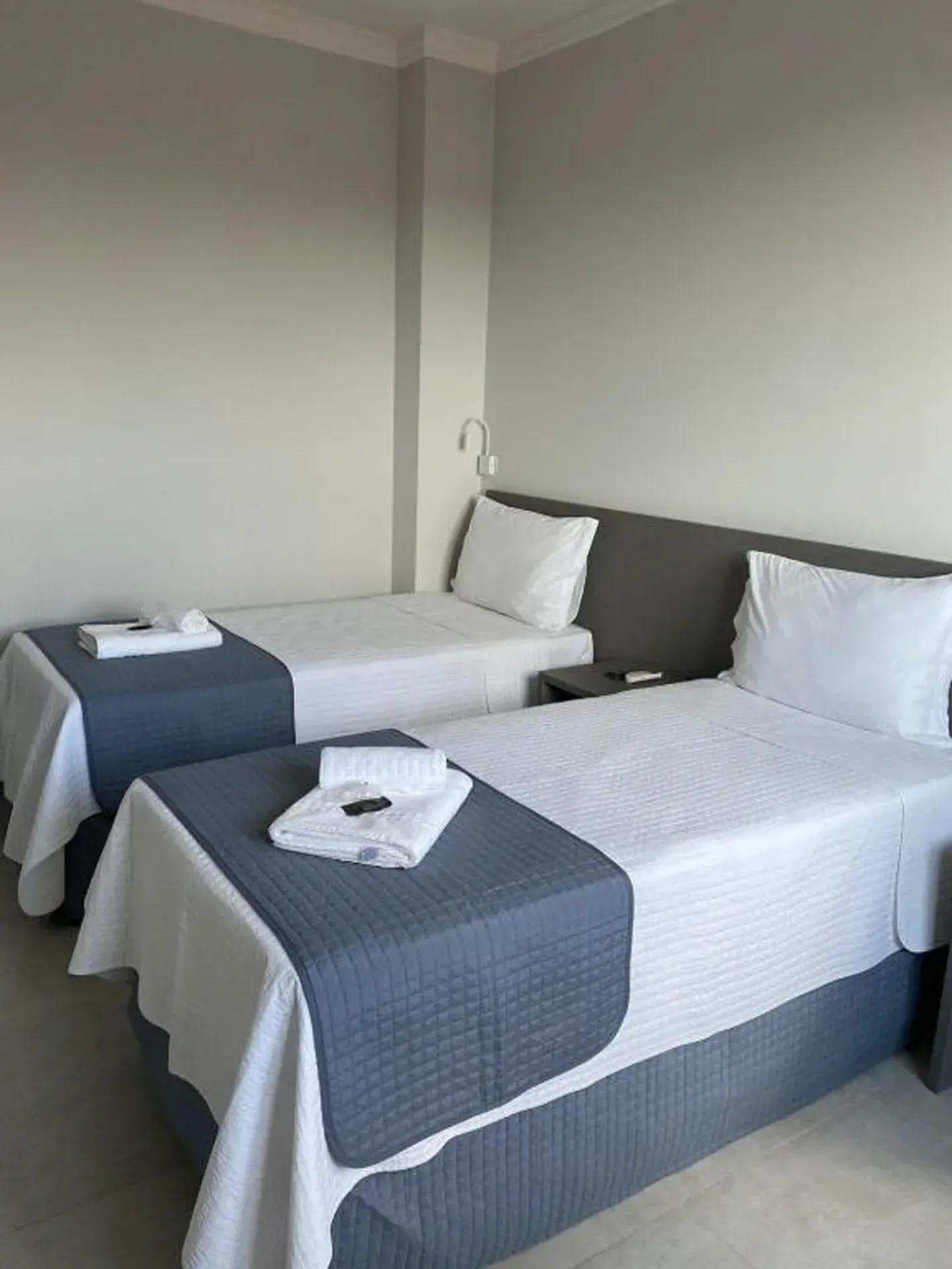 Duas camas de solteiro em um quarto de hotel com lençóis brancos e peseiras cinza.