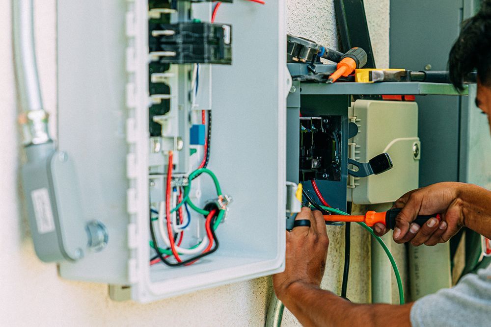 A man is working on an electrical box with a screwdriver.