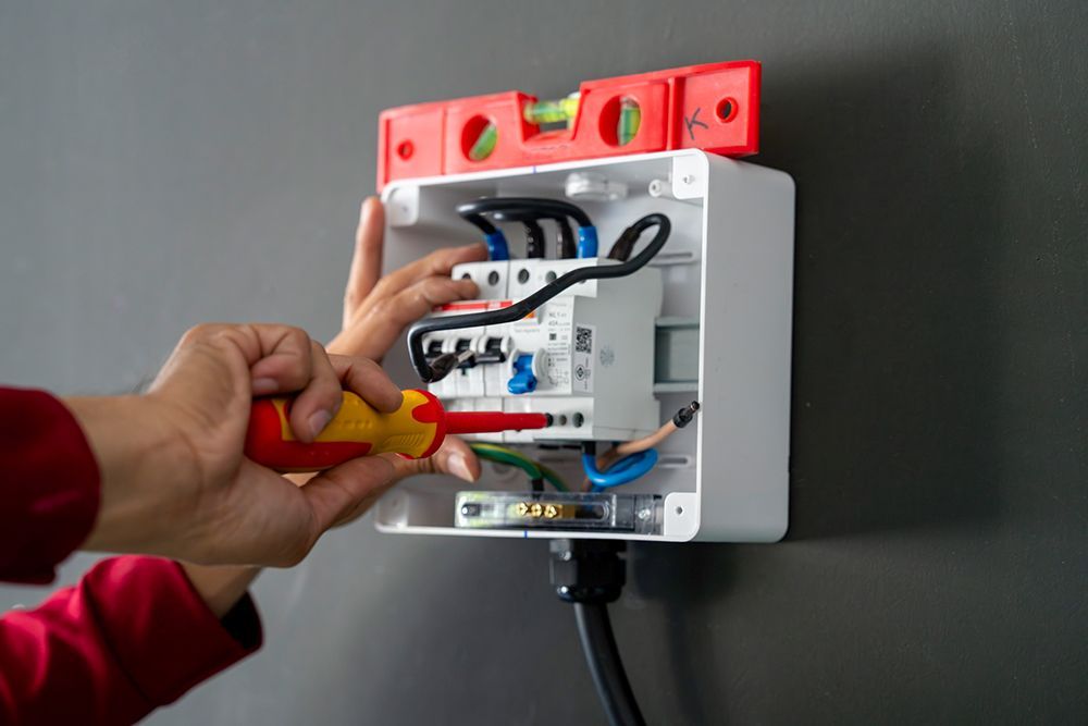 A person is working on an electrical box with a screwdriver.