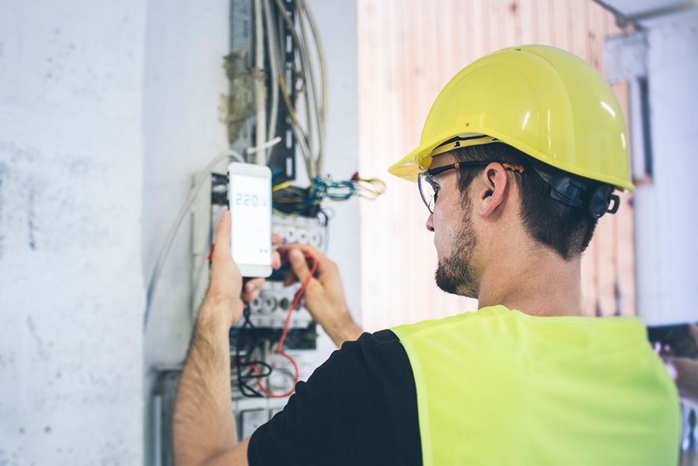 A man wearing a hard hat and safety vest is working on an electrical box.