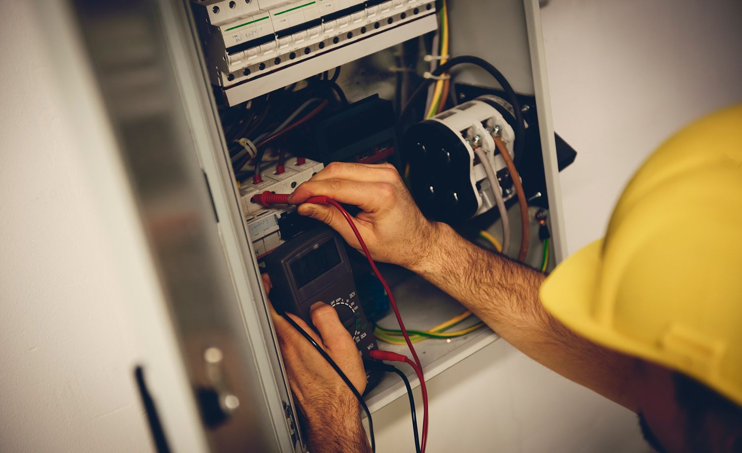 A man in a yellow hard hat is working on an electrical box.