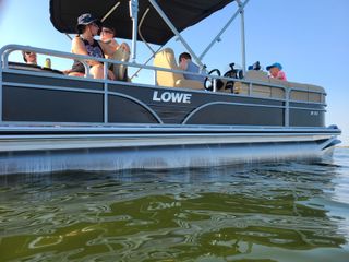 A group of people are riding a pontoon boat on a lake.