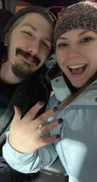 A man and a woman are posing for a picture . the woman is wearing a ring on her finger.