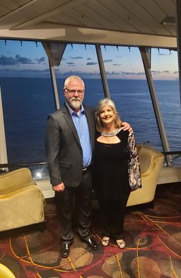 A man and a woman are posing for a picture in front of a large window overlooking the ocean.