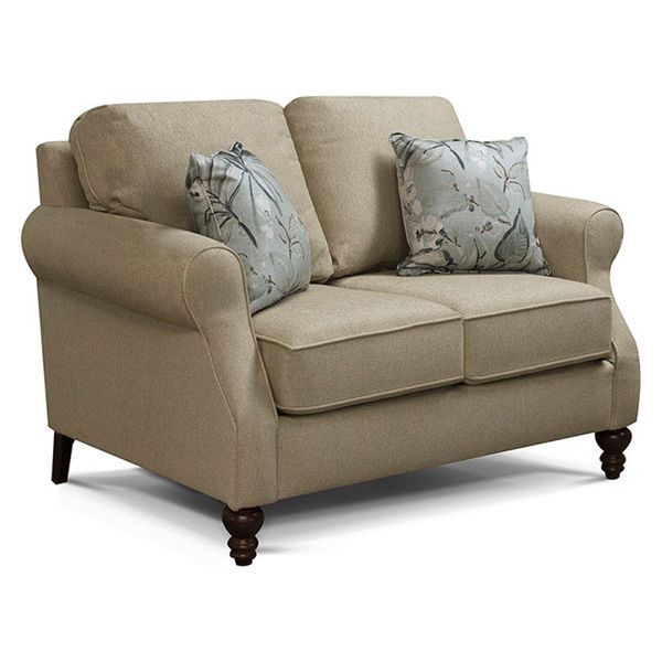 Beige loveseat with two light patterned pillows and dark wooden legs on a white background