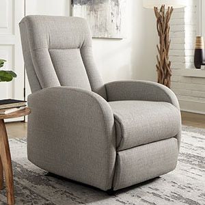 Light gray upholstered recliner chair in a bright living room with a rug and wooden side table