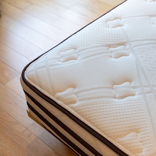 Close-up of a white quilted mattress corner with brown side stripes on a wooden floor
