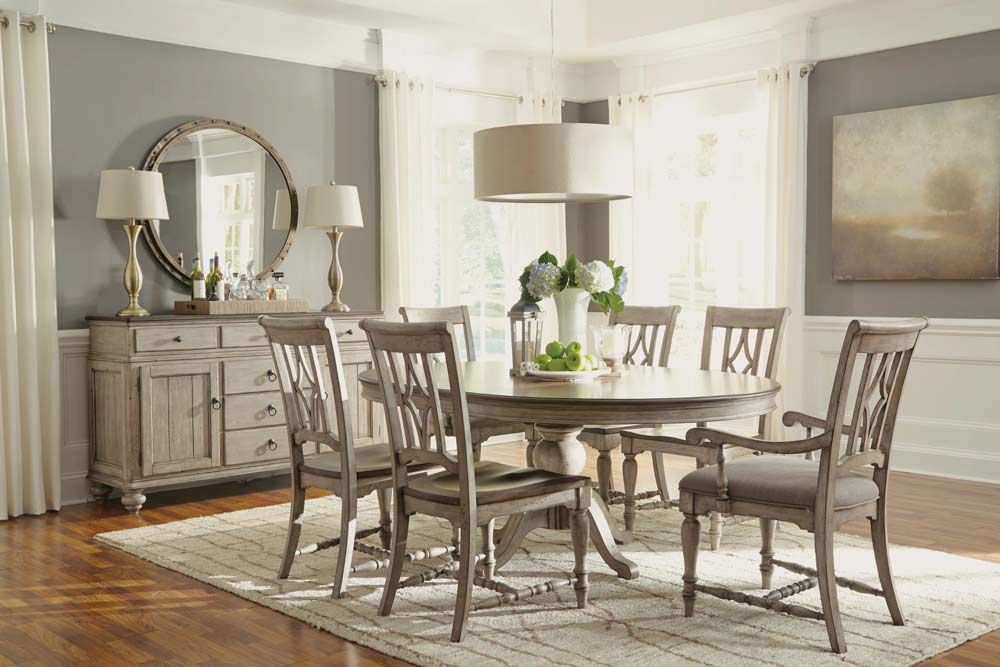 Bright dining room with a wooden table, six chairs, sideboard, mirror, lamp, and rug.