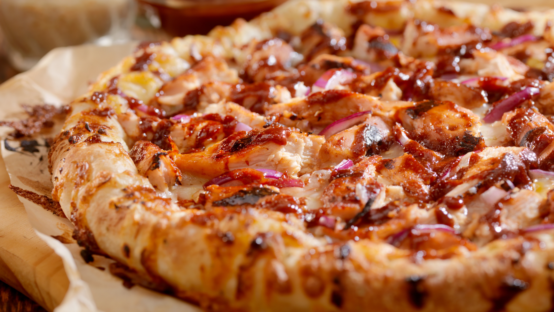 A pizza with chicken , bacon and onions on a wooden cutting board.
