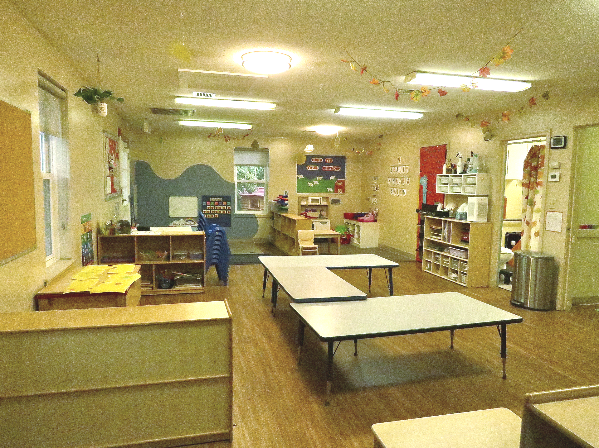 A large room filled with cribs , tables , chairs and a bouncer.