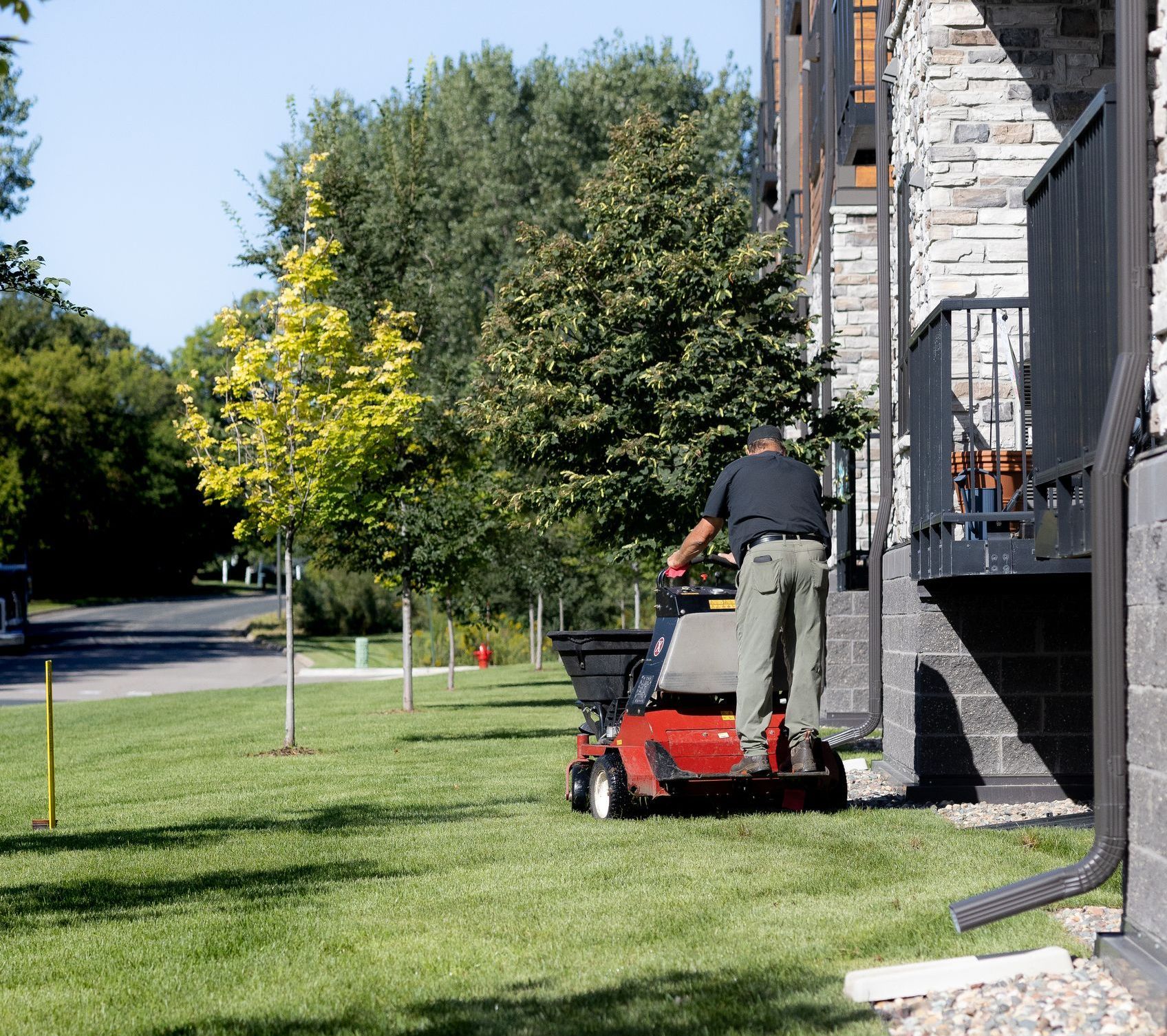 A man is mowing a lush green lawn in front of a building