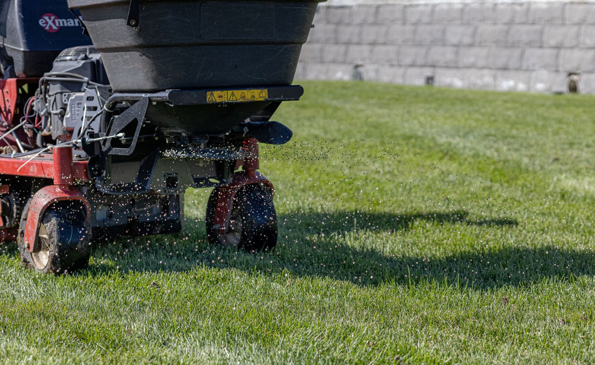 A person is using a lawn mower to spread fertilizer on a lush green lawn.