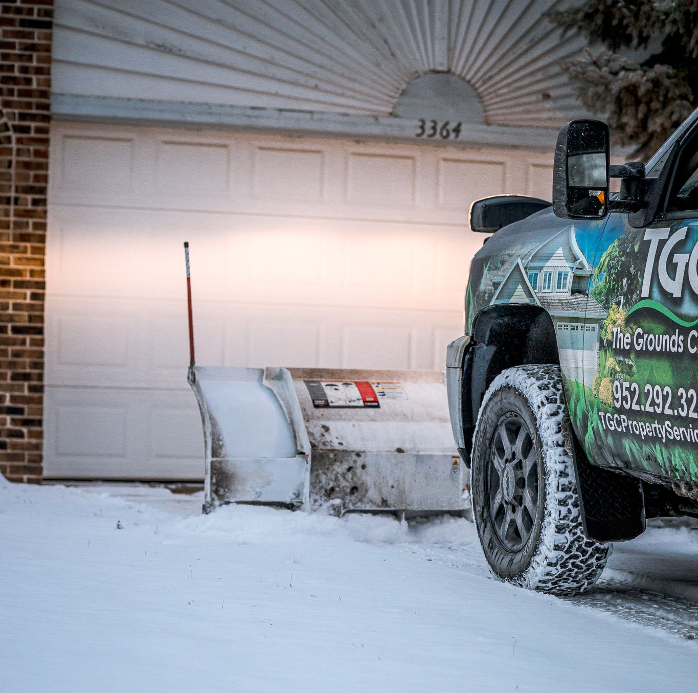 Snowplow clearing snow from a driveway in front of a white garage door.