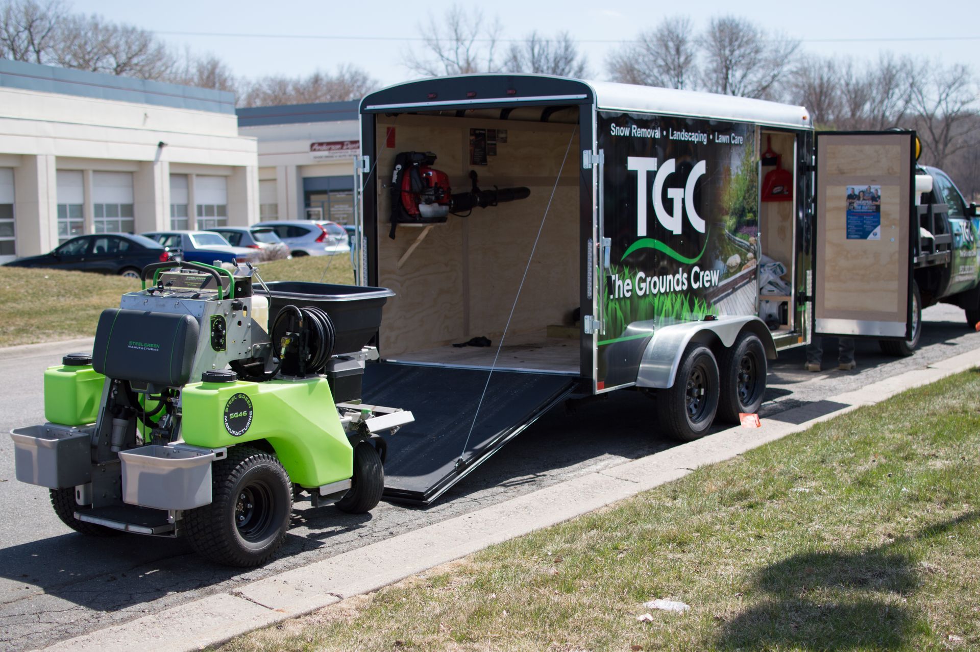 A green lawn mower is parked next to a trailer that says tgc