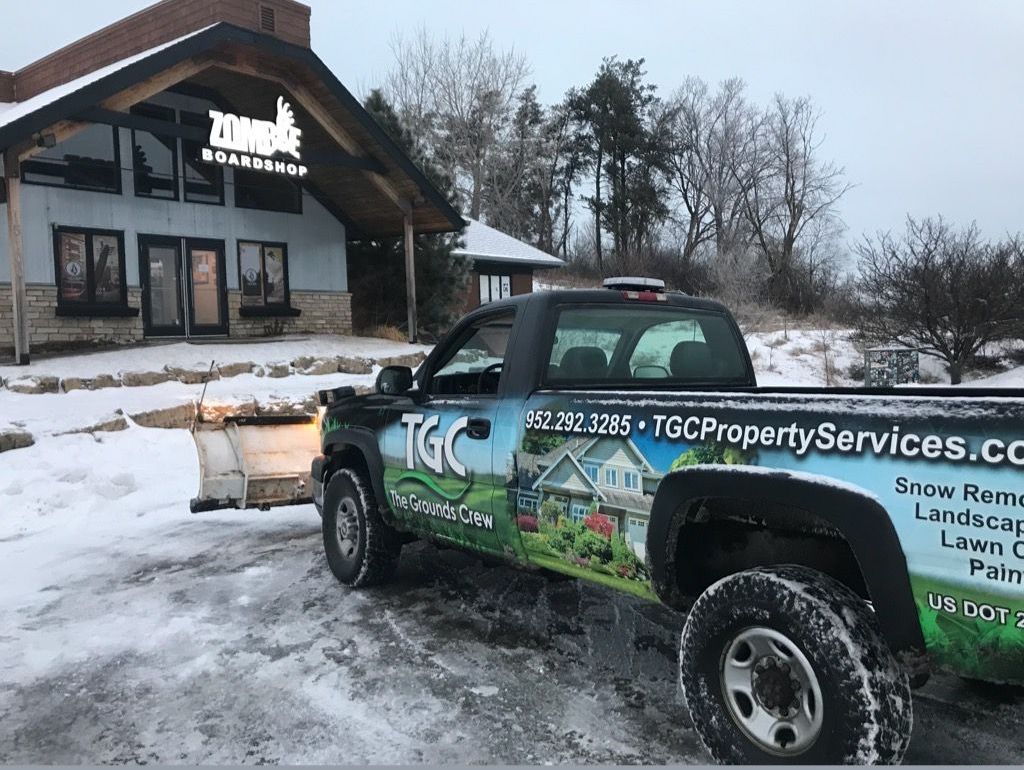 A TGC truck with a plow attached to it is parked in front of a house.