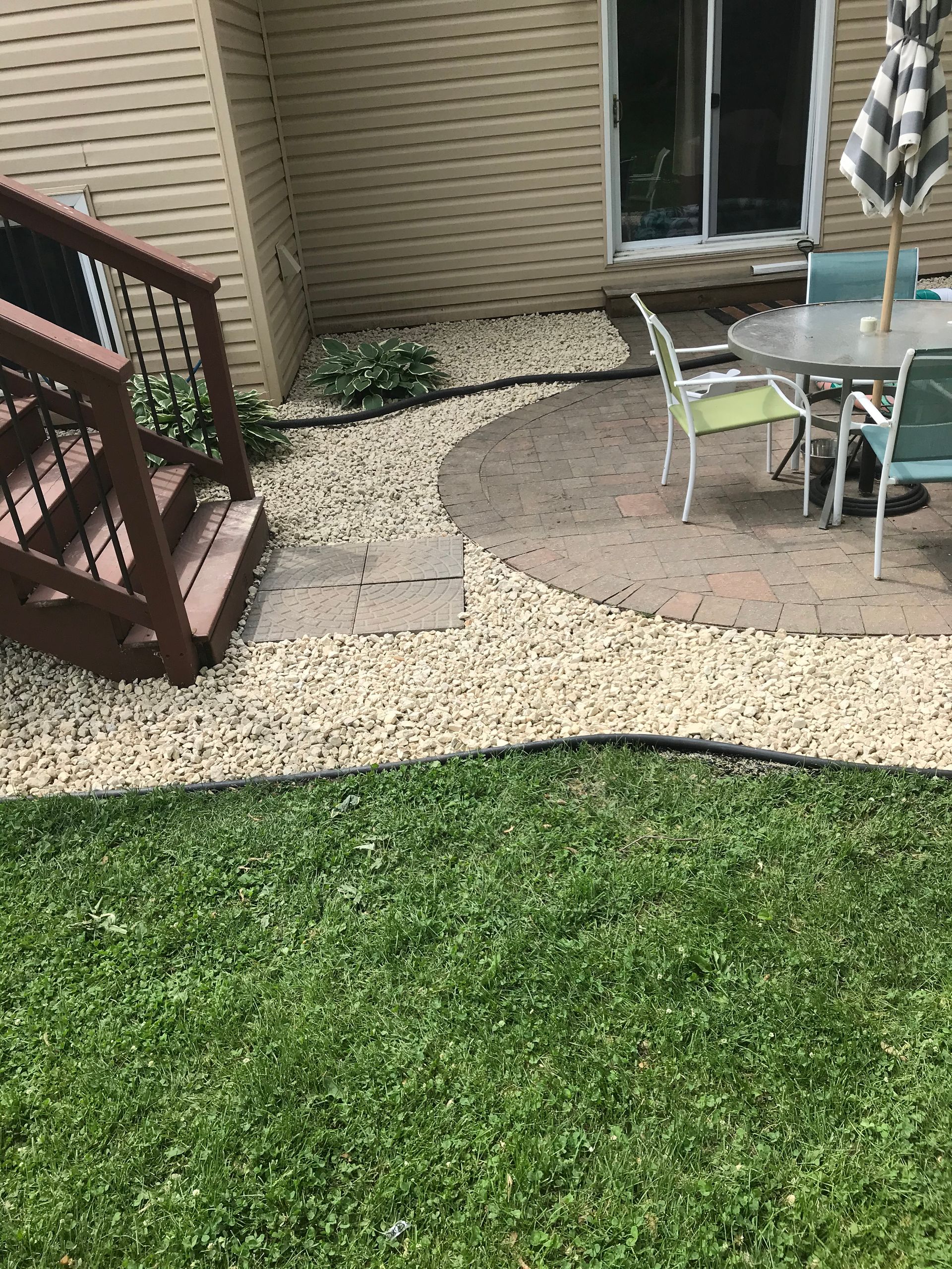 Backyard with a brick patio, gravel path, and wooden stairs leading to a house.