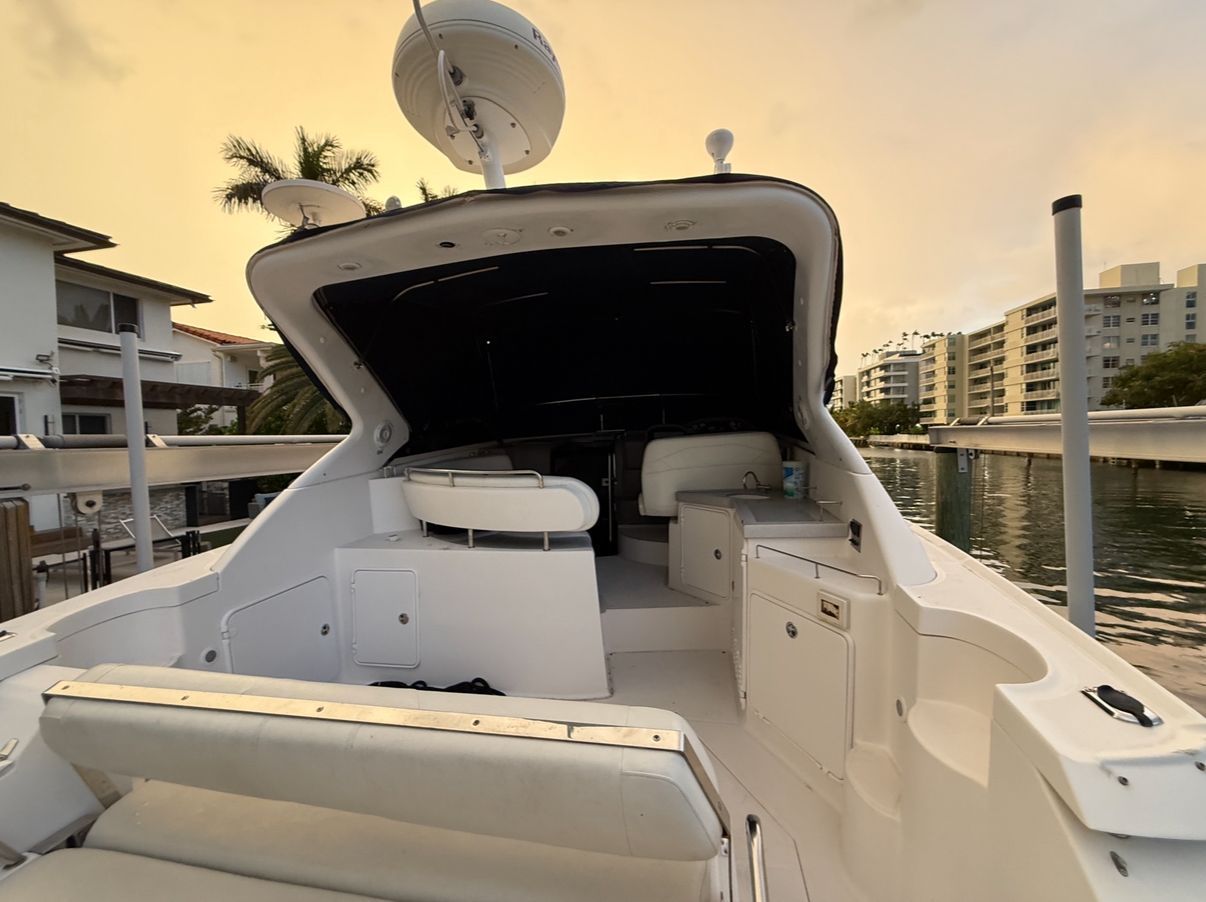 A white yacht stern with seating, radar, and a canal view at sunset.