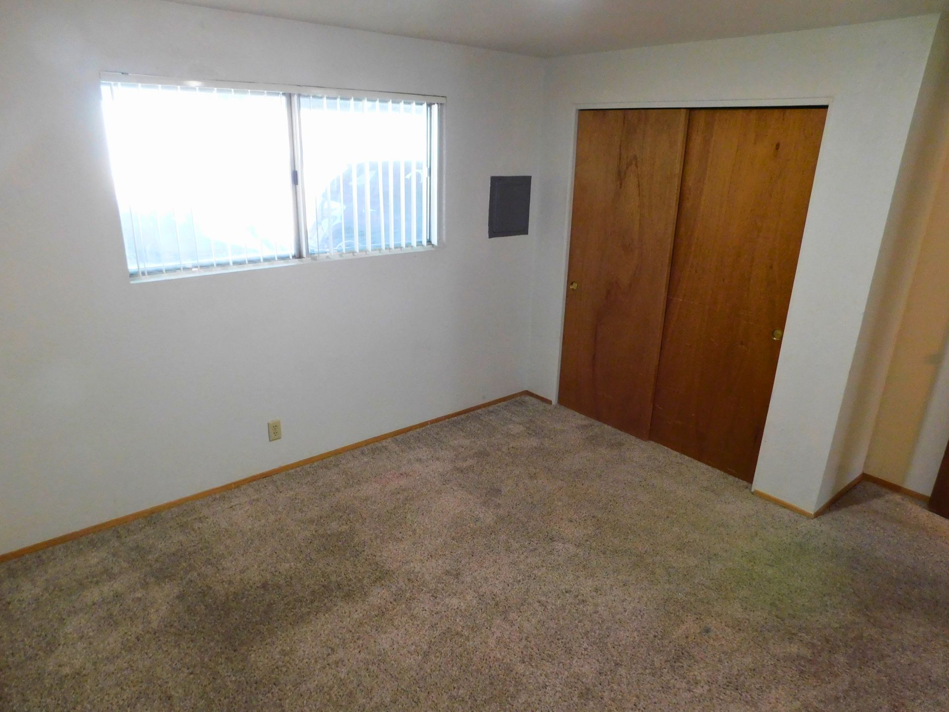 Empty bedroom with neutral carpet, white walls, a window, and a closet.