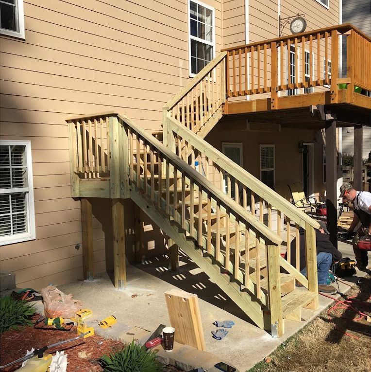 Wooden stairs lead from a deck to the ground. Two men work nearby.