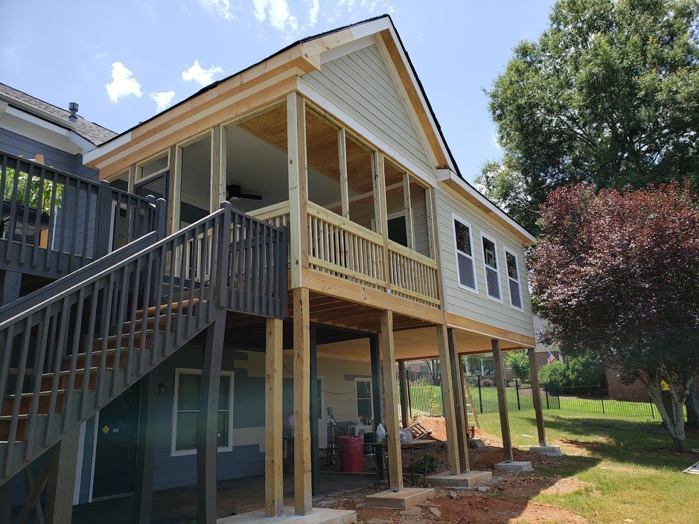 A two-story house with a wooden deck and screened-in porch under construction against a blue sky.