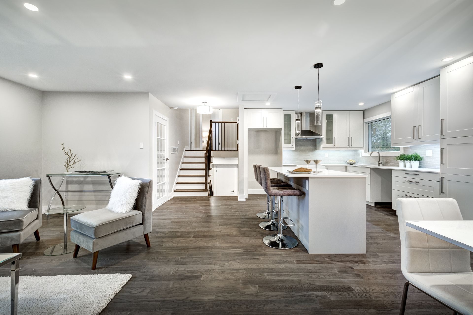 Modern open-concept home interior with hardwood floors, white kitchen, living area, and staircase.