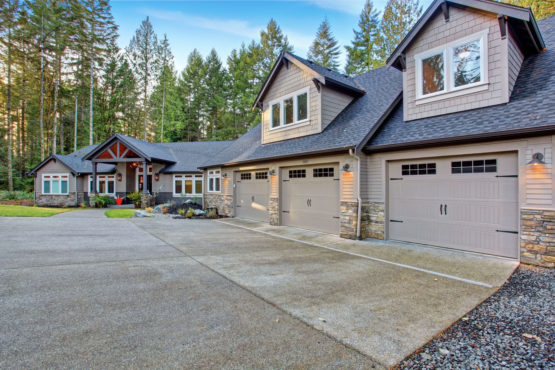 Beige house with three-car garage, concrete driveway, and forested background.
