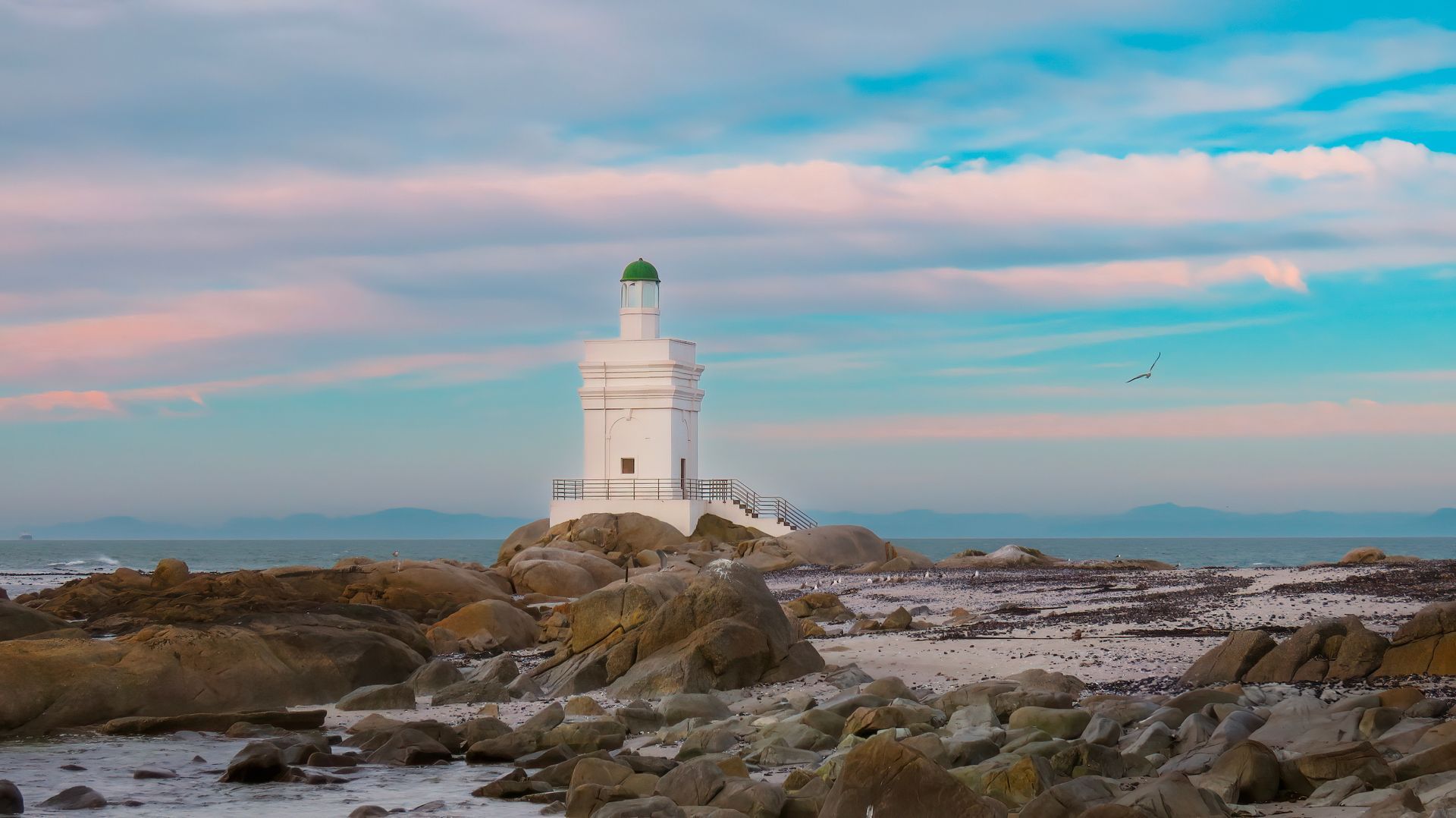 A white lighthouse is sitting on top of a rocky island near the ocean.