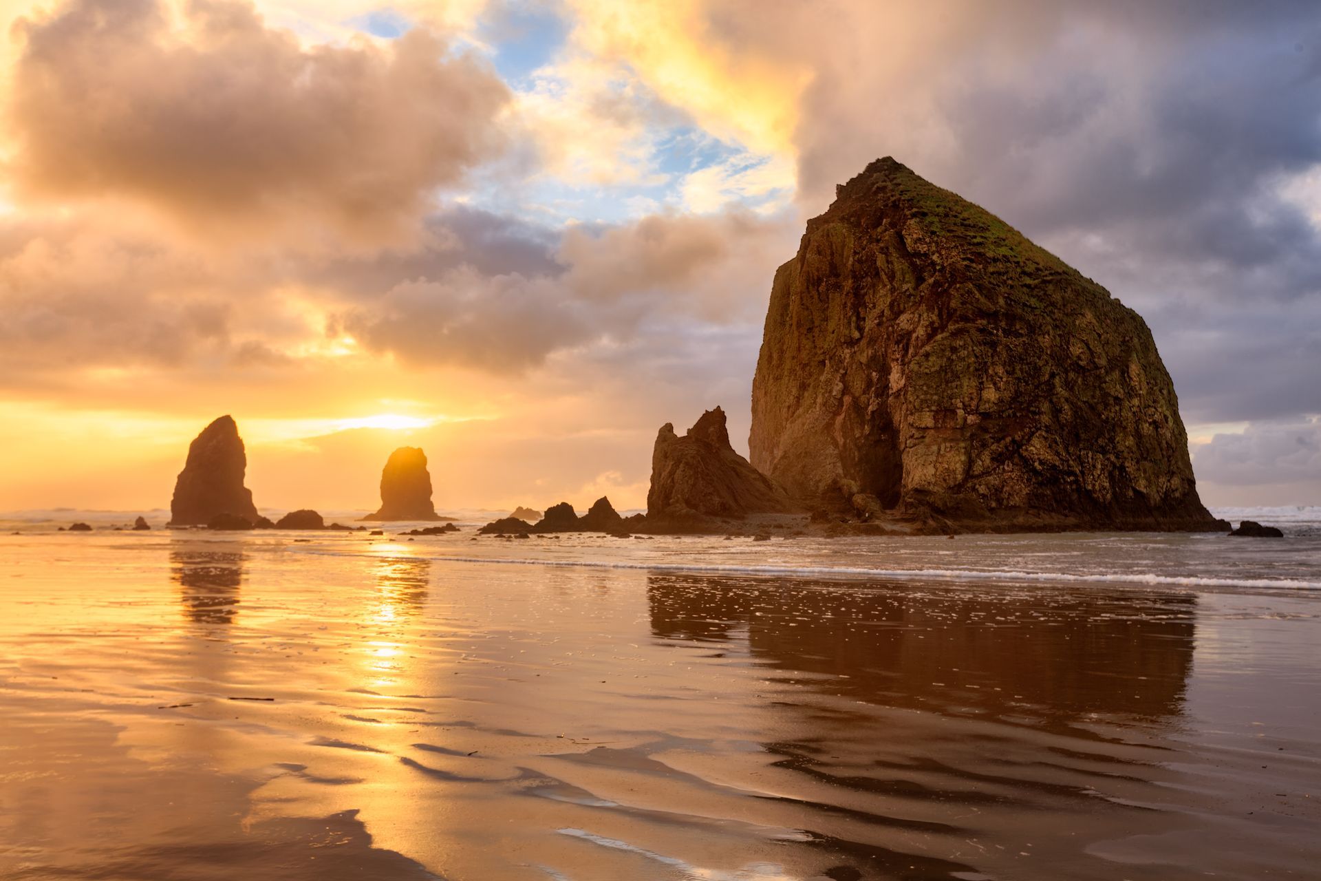 Golden sunset over Cannon Beach, Oregon. Large sea stacks reflect in the wet sand.