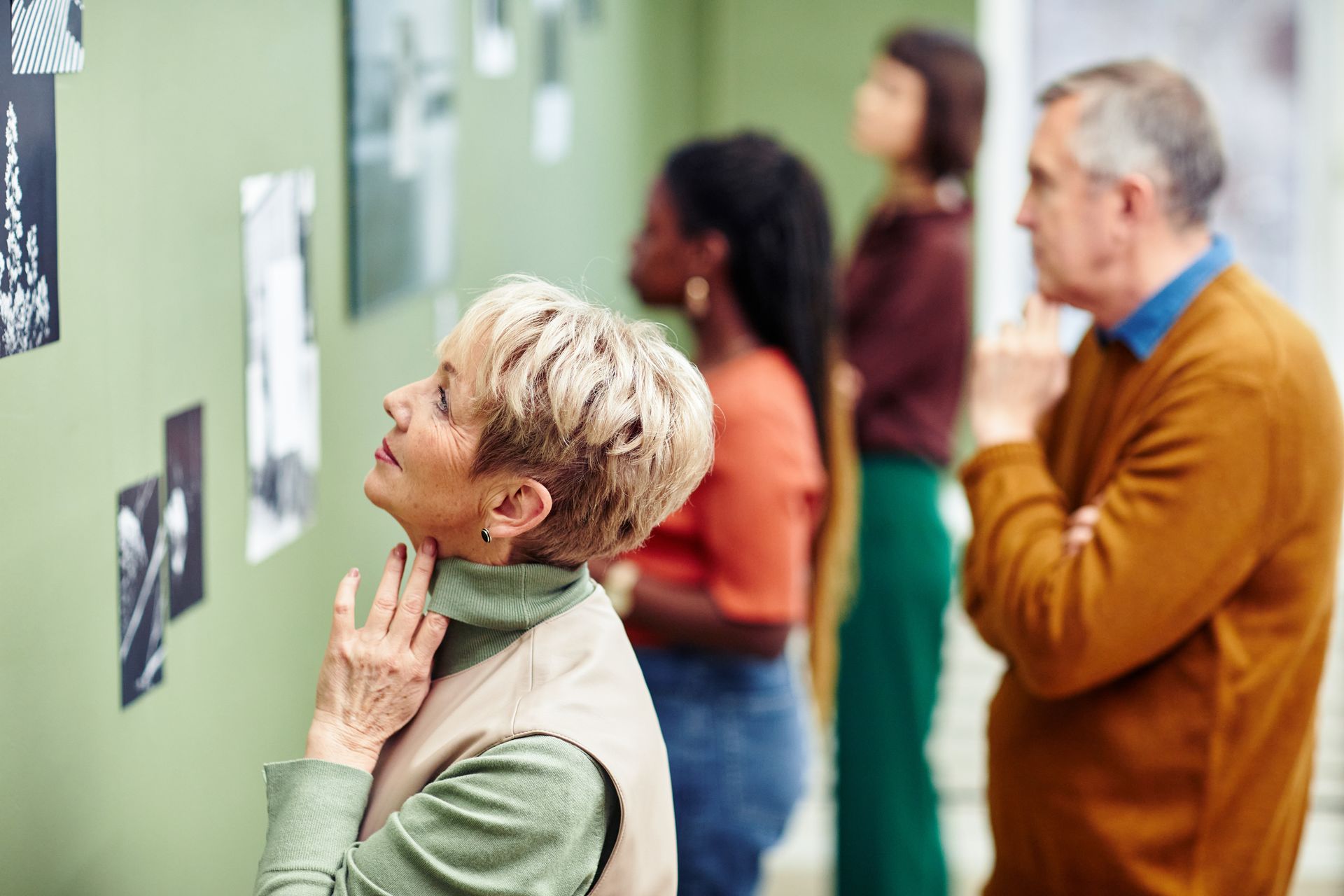 A group of people are looking at paintings on a wall in a museum.