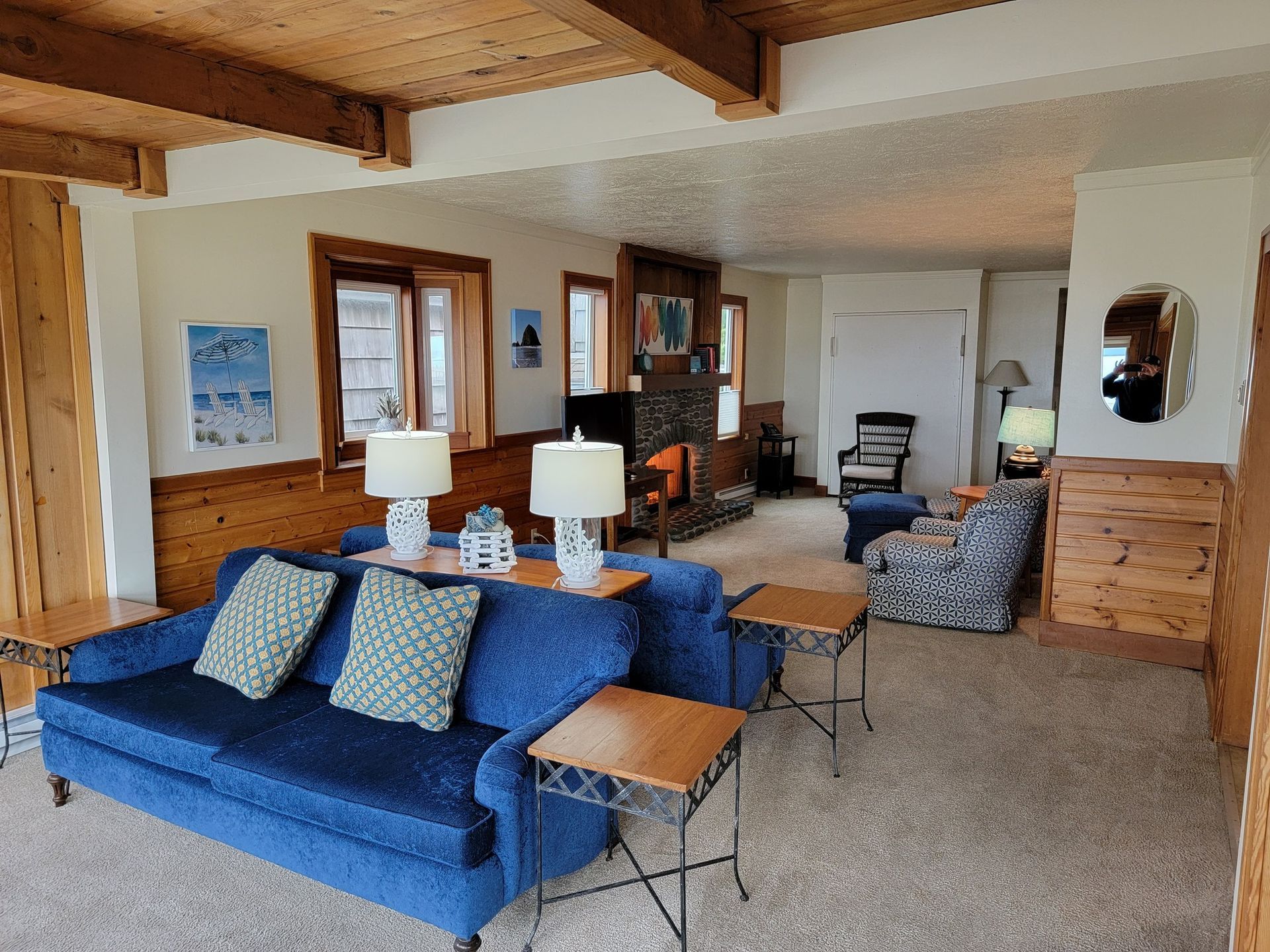 A living room with a blue couch , chairs , lamps and a fireplace.