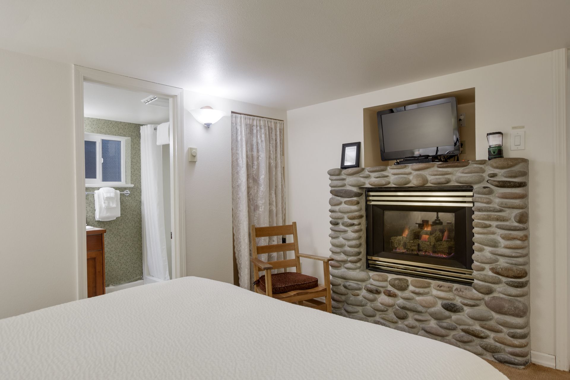 A bedroom with a bed , chair , fireplace and television.
