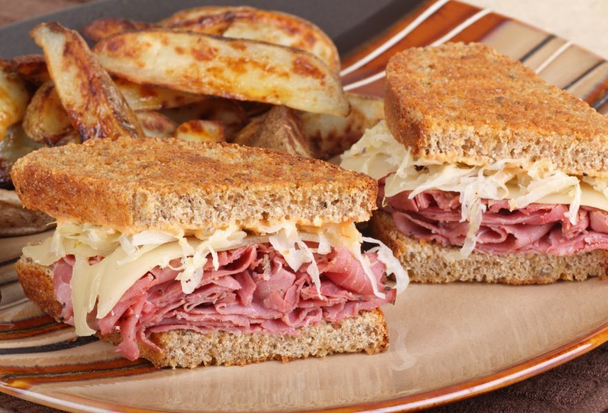 Two corned beef sandwiches with french fries on a plate.