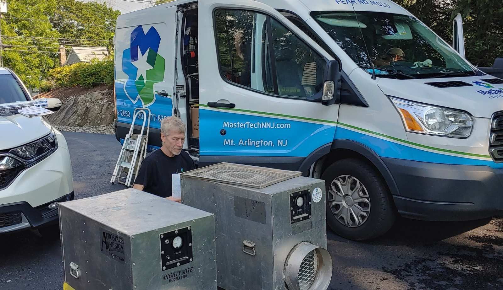 A man is standing in front of a van with two boxes in front of it.