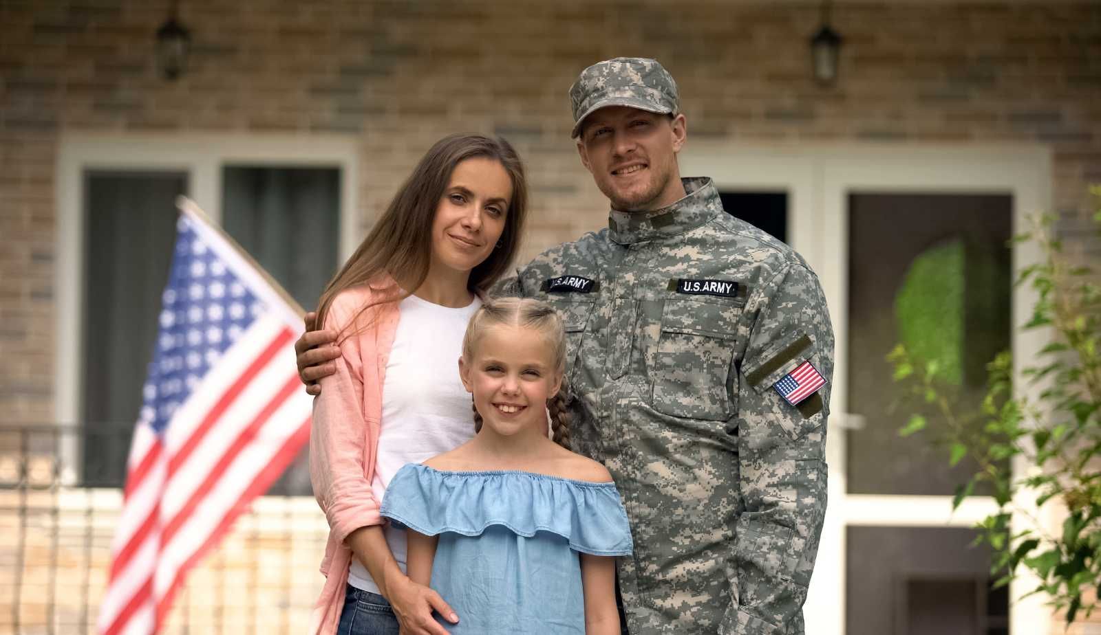 A soldier and his family are posing for a picture in front of their house.