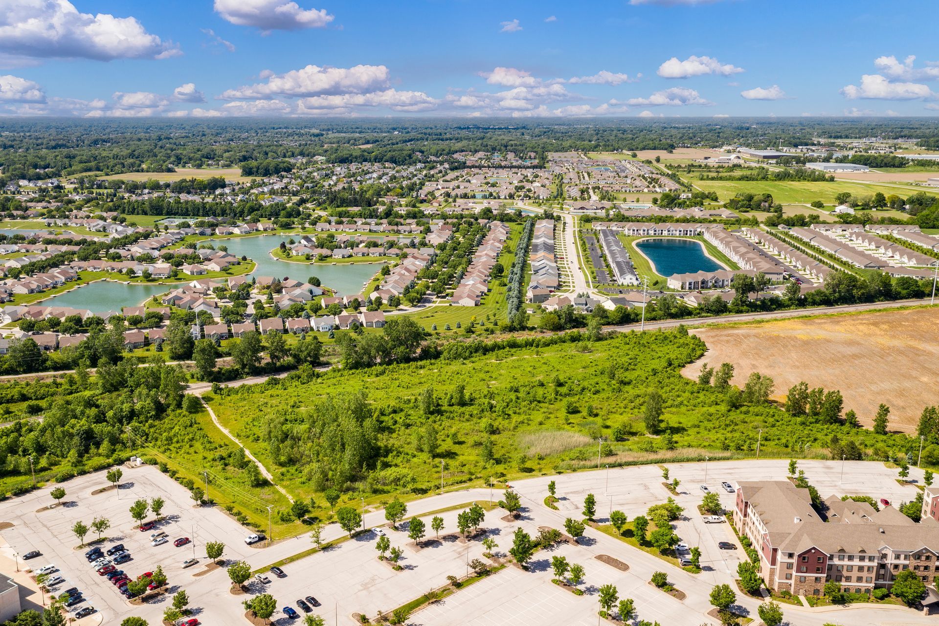 Aerial view of a residential area with houses, ponds, trees, and parking lots under a blue sky.