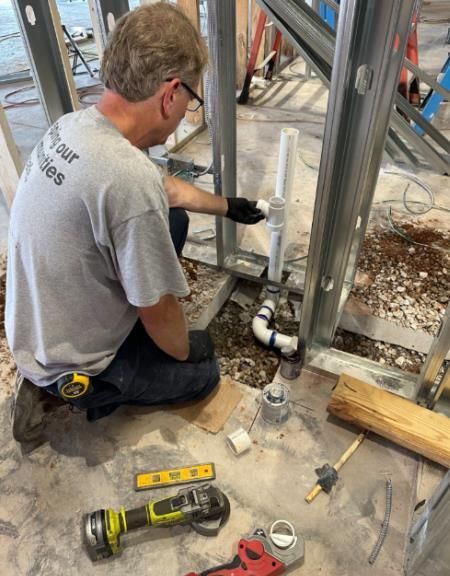 A man wearing a grey shirt that says repair tables is working on a pipe
